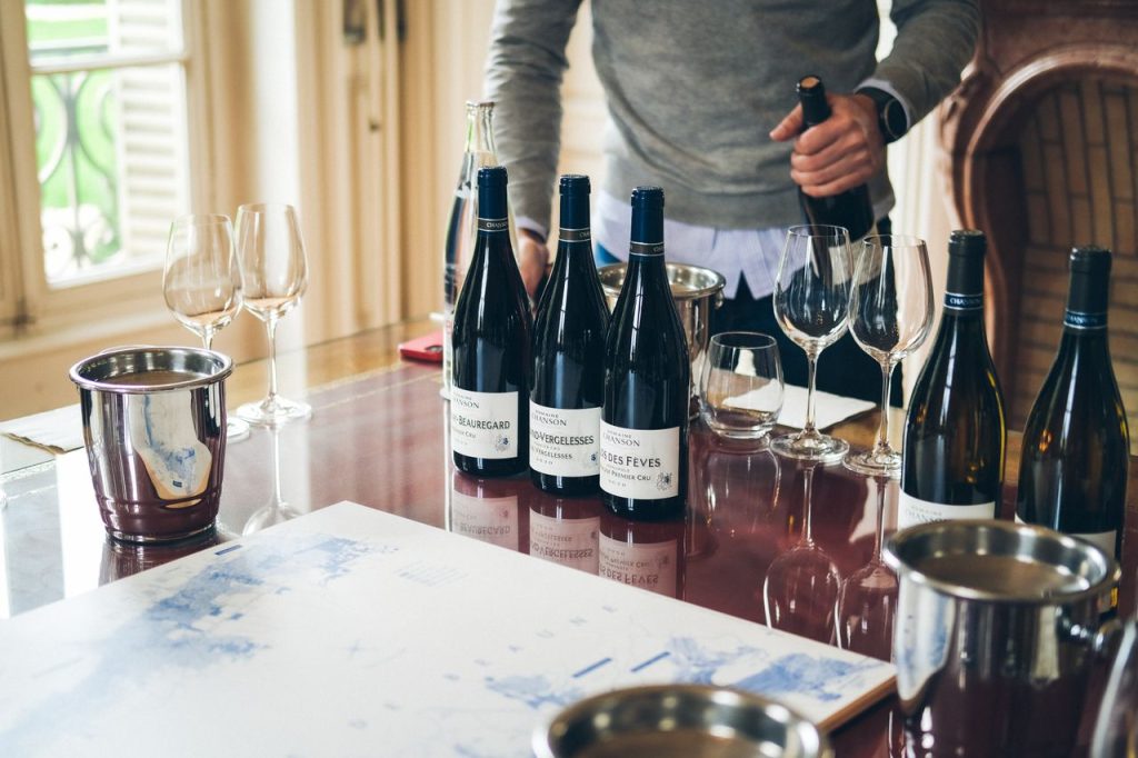 A sommelier pouring wine from bottles on a restaurant table with glasses and buckets.