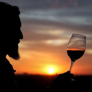 Silhouette of a bearded man holding a glass of wine against a vibrant sunset in Buenos Aires.